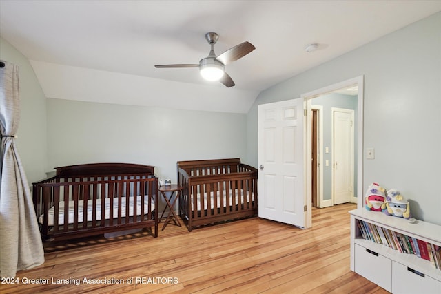 bedroom featuring vaulted ceiling, ceiling fan, light hardwood / wood-style flooring, and a crib