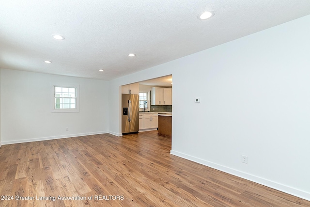 unfurnished living room featuring a textured ceiling, light hardwood / wood-style flooring, and sink