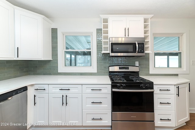 kitchen with white cabinets, decorative backsplash, light stone counters, and appliances with stainless steel finishes