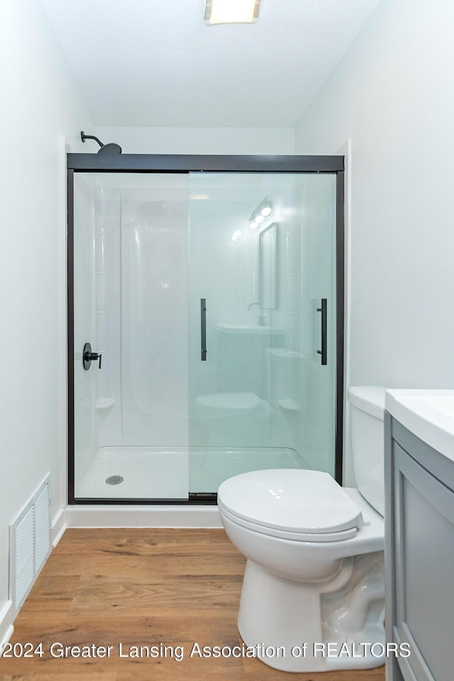 bathroom featuring wood-type flooring, vanity, toilet, and a shower with door