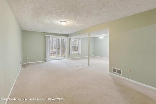 basement featuring light carpet, ceiling fan, and a textured ceiling