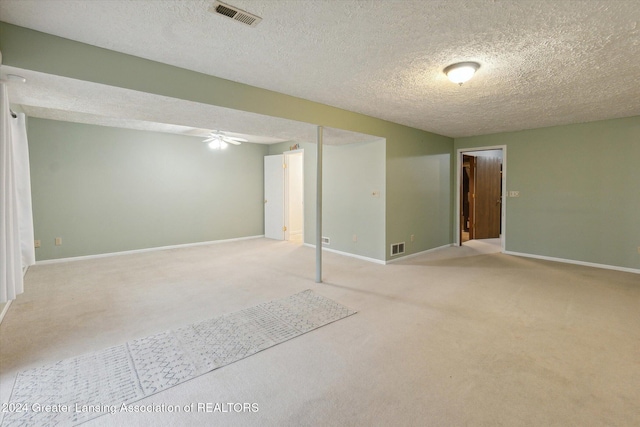 basement featuring ceiling fan, light colored carpet, and a textured ceiling