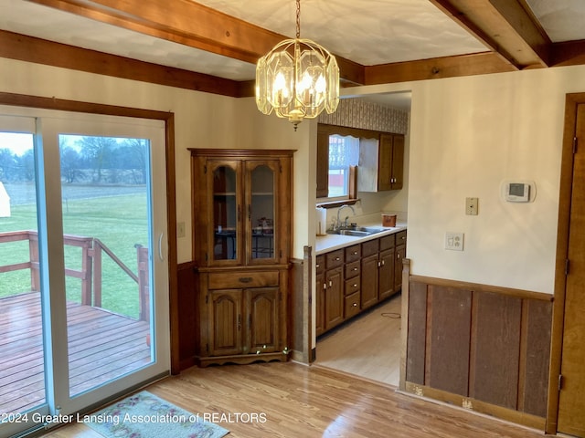 kitchen featuring sink, hanging light fixtures, light hardwood / wood-style flooring, beamed ceiling, and a notable chandelier