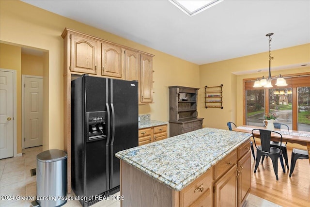 kitchen featuring pendant lighting, a center island, black fridge, light stone countertops, and a notable chandelier