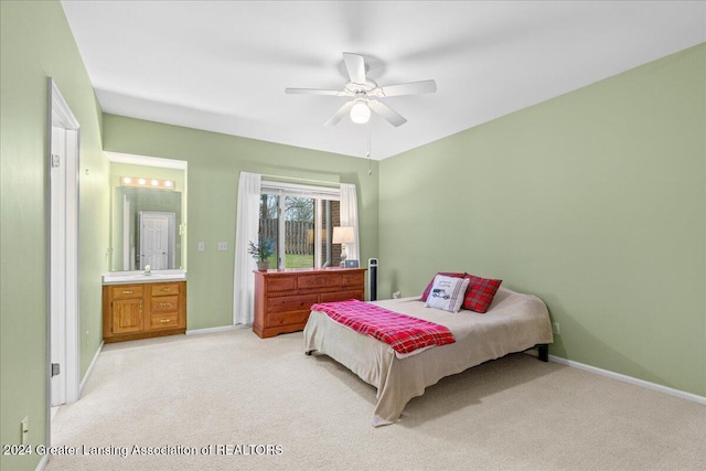 bedroom with ceiling fan, light colored carpet, and ensuite bath