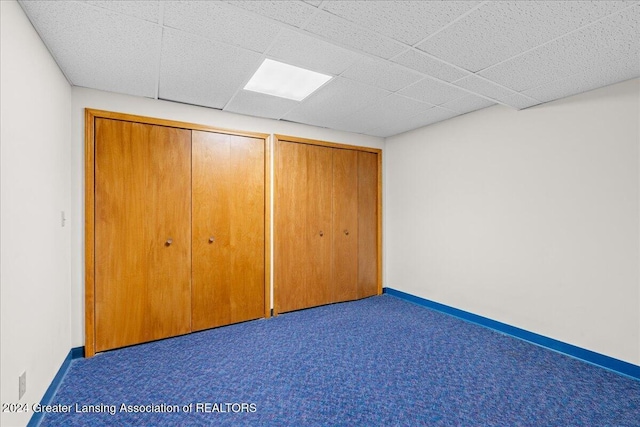 unfurnished bedroom featuring carpet flooring, multiple closets, and a drop ceiling