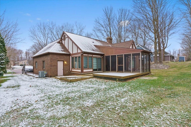 snow covered back of property with a sunroom, cooling unit, a wooden deck, and a lawn