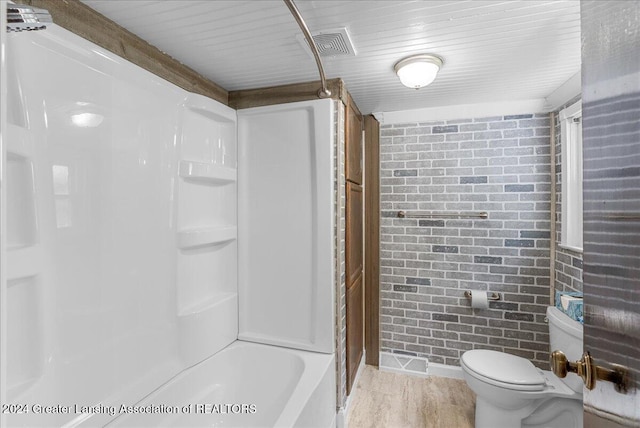 bathroom with wood-type flooring, brick wall, shower / bathtub combination, and toilet