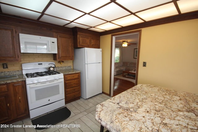 kitchen with ceiling fan, light stone counters, white appliances, and backsplash