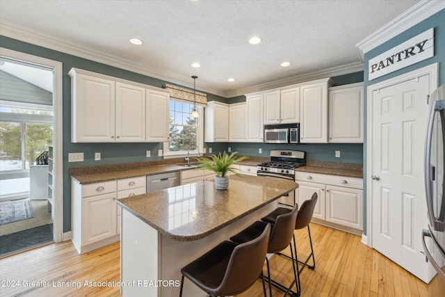 kitchen featuring appliances with stainless steel finishes, sink, decorative light fixtures, white cabinetry, and a kitchen island