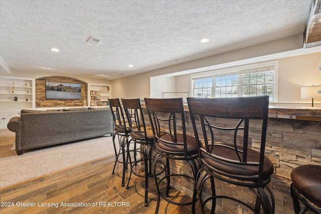 dining space featuring hardwood / wood-style floors, built in features, a textured ceiling, and indoor bar