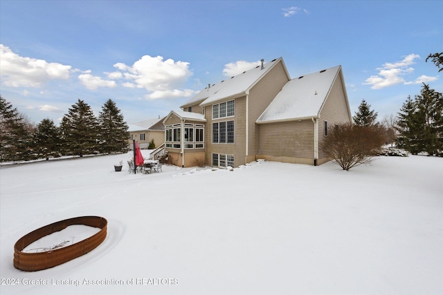 snow covered back of property featuring a sunroom