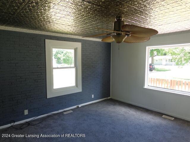 carpeted spare room with ceiling fan and brick wall