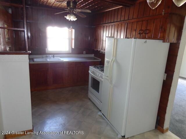 kitchen with ceiling fan, sink, white appliances, and wooden walls