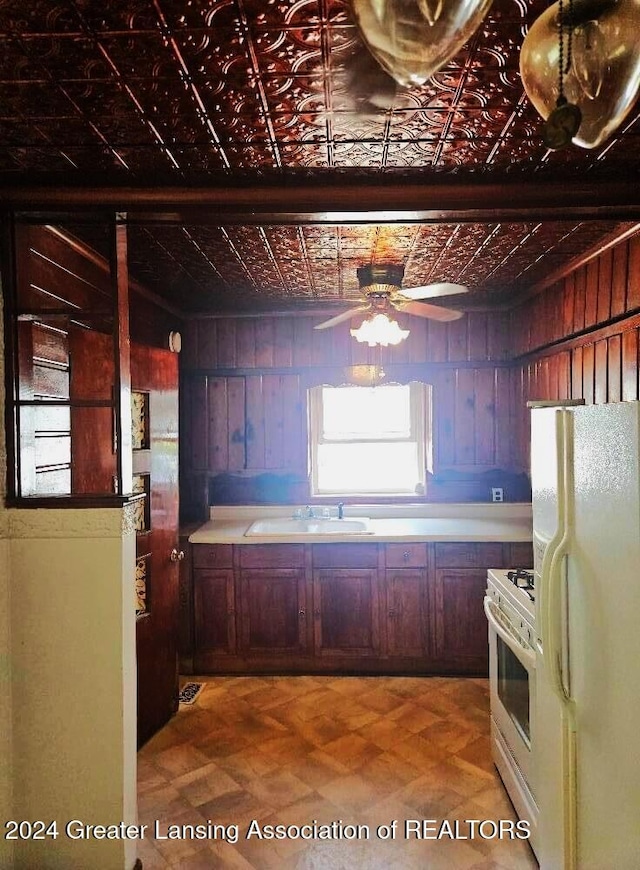 kitchen featuring ceiling fan, sink, white refrigerator, wood walls, and range