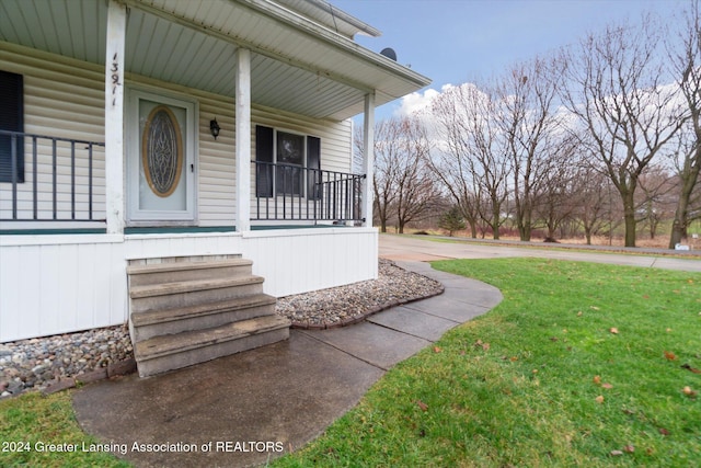 view of exterior entry featuring a porch and a lawn