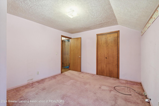 unfurnished bedroom featuring carpet flooring, a closet, a textured ceiling, and lofted ceiling