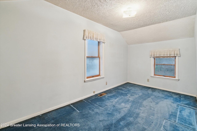 carpeted spare room with a textured ceiling and vaulted ceiling