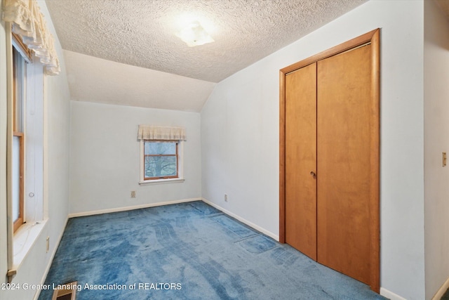 unfurnished bedroom with carpet flooring, a closet, a textured ceiling, and lofted ceiling