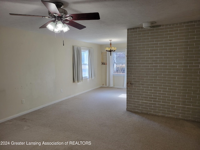 spare room featuring carpet, ceiling fan with notable chandelier, a textured ceiling, and brick wall