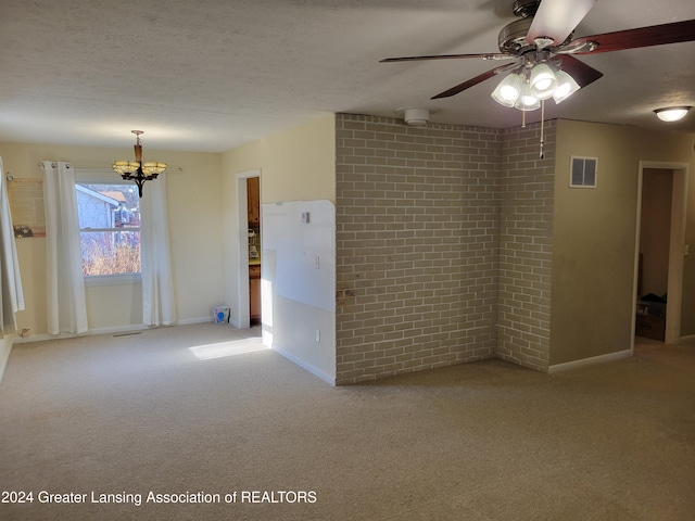 carpeted empty room with a textured ceiling, brick wall, and ceiling fan with notable chandelier