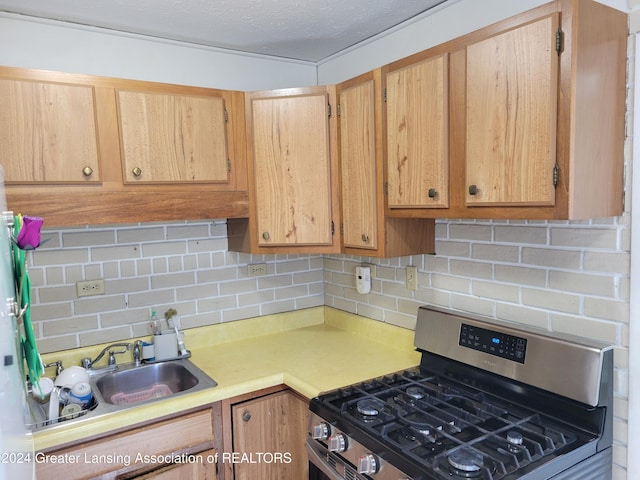 kitchen with light brown cabinetry, backsplash, stainless steel gas range oven, and sink