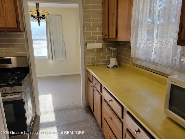 kitchen with a chandelier, tasteful backsplash, light colored carpet, and stainless steel range with gas stovetop