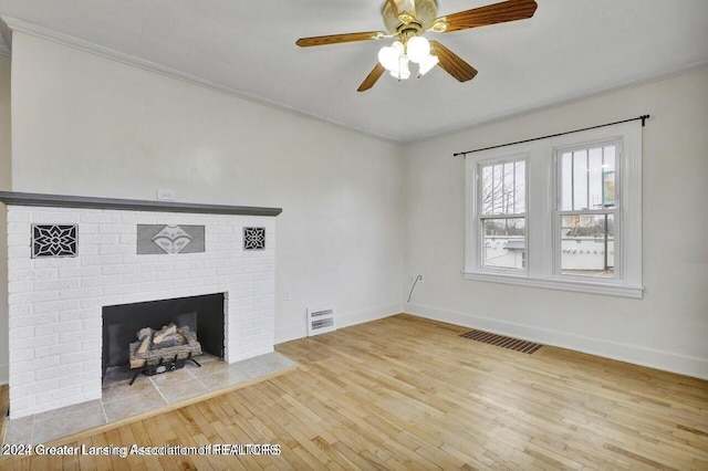 unfurnished living room with hardwood / wood-style flooring, ceiling fan, ornamental molding, and a brick fireplace