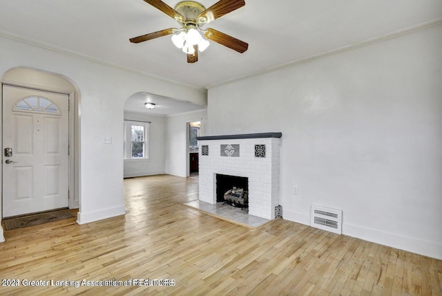 unfurnished living room with light hardwood / wood-style floors, a brick fireplace, ceiling fan, and crown molding