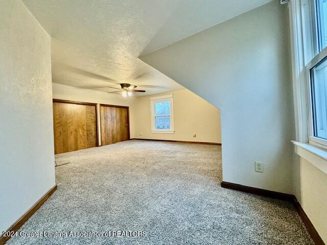 bonus room featuring a textured ceiling, ceiling fan, carpet floors, and lofted ceiling