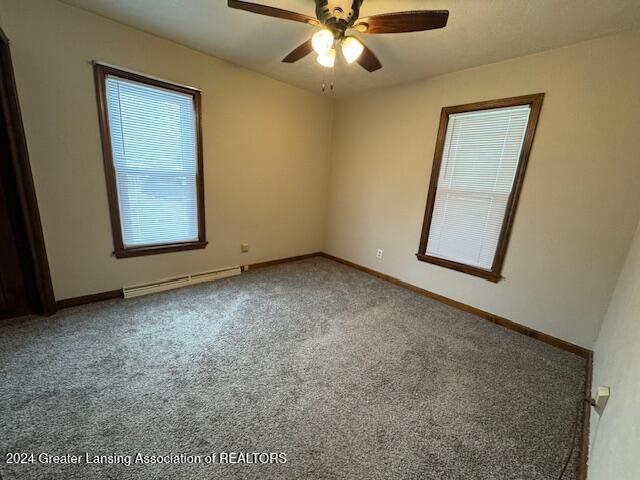 carpeted spare room featuring plenty of natural light, baseboard heating, and ceiling fan