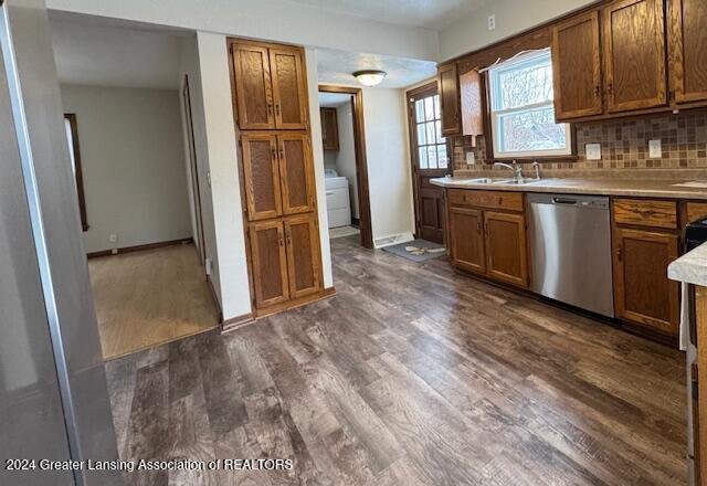 kitchen featuring sink, stainless steel dishwasher, dark hardwood / wood-style floors, decorative backsplash, and washer / dryer