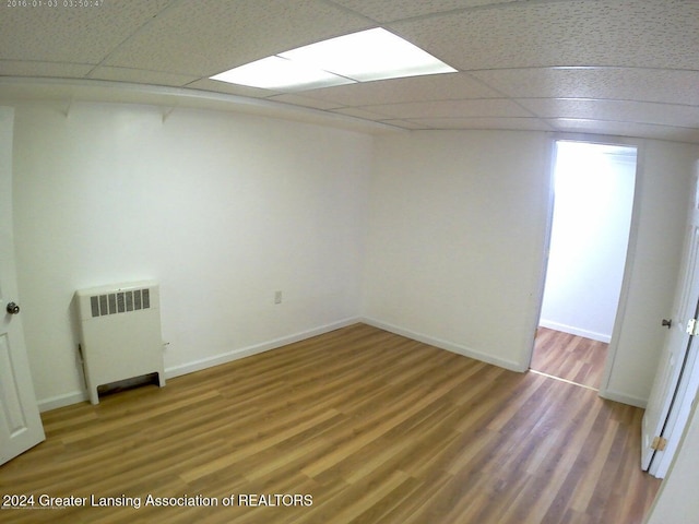 empty room featuring radiator, hardwood / wood-style floors, and a drop ceiling