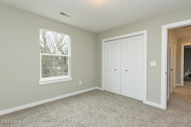 unfurnished bedroom featuring a textured ceiling, light carpet, and a closet