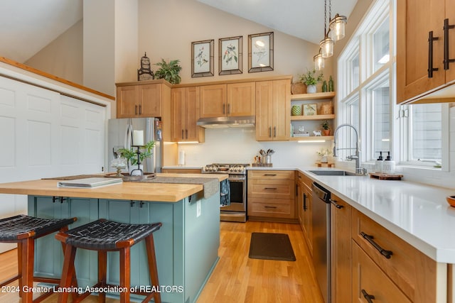 kitchen featuring stainless steel appliances, sink, butcher block countertops, a kitchen island, and hanging light fixtures