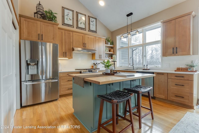 kitchen with stainless steel appliances, vaulted ceiling, pendant lighting, a center island, and butcher block counters