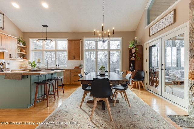 dining space with sink, french doors, an inviting chandelier, lofted ceiling, and light wood-type flooring