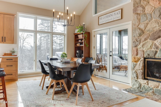 dining space with a notable chandelier, a stone fireplace, light wood-type flooring, and french doors