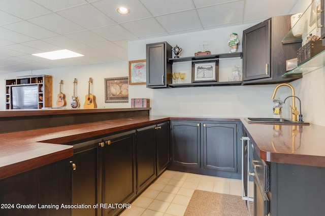 kitchen with a paneled ceiling, dark brown cabinetry, sink, and light tile patterned floors