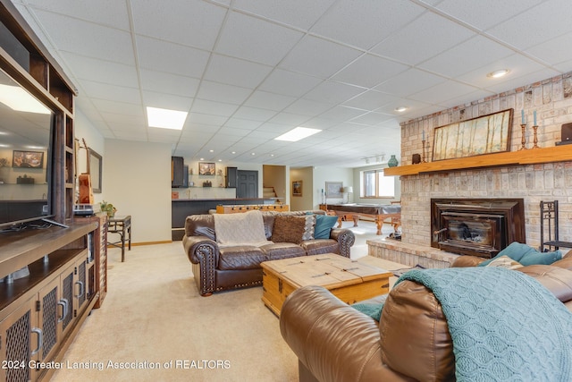 carpeted living room featuring a drop ceiling and a brick fireplace