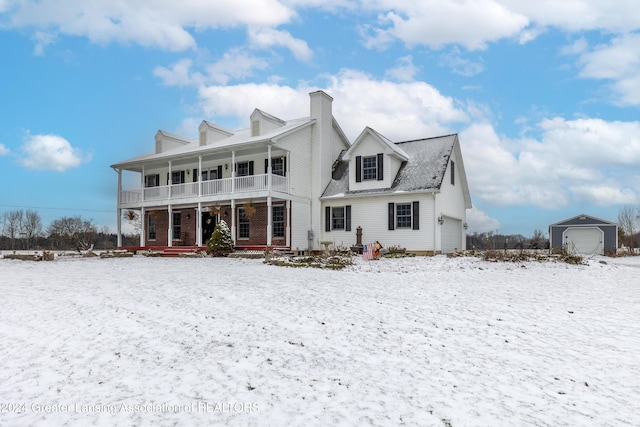 snow covered rear of property featuring a porch, a garage, and an outbuilding