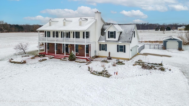 snow covered property featuring covered porch, a garage, and an outdoor structure