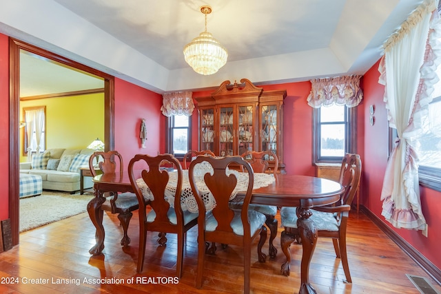 dining room featuring a healthy amount of sunlight, wood-type flooring, a tray ceiling, and an inviting chandelier