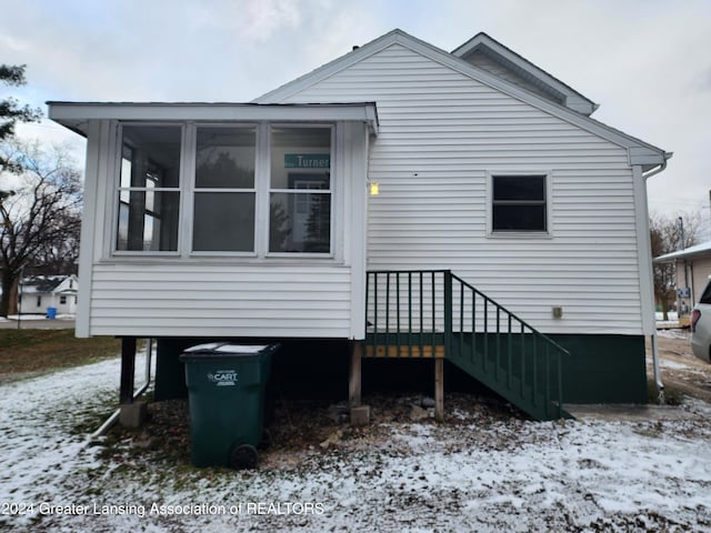 snow covered back of property featuring a sunroom