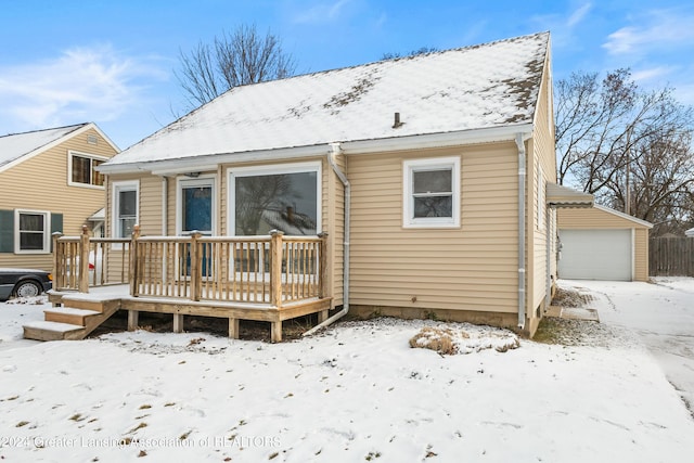 snow covered house with a wooden deck, an outbuilding, and a garage