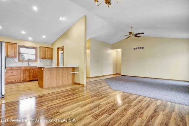 kitchen featuring stainless steel refrigerator, kitchen peninsula, light hardwood / wood-style floors, decorative backsplash, and ceiling fan with notable chandelier