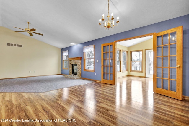 unfurnished living room with french doors, light hardwood / wood-style floors, lofted ceiling, a fireplace, and ceiling fan with notable chandelier