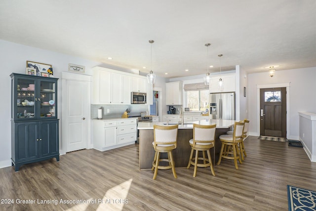 kitchen featuring stainless steel appliances, a kitchen island with sink, dark wood-type flooring, white cabinetry, and hanging light fixtures