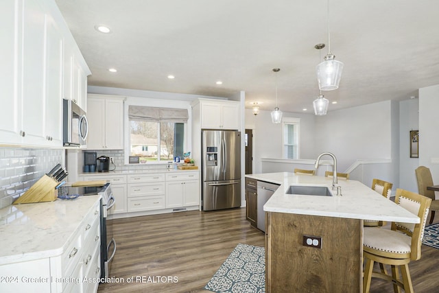 kitchen with pendant lighting, a kitchen island with sink, sink, appliances with stainless steel finishes, and white cabinetry