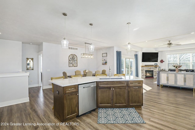 kitchen featuring ceiling fan, dishwasher, sink, a stone fireplace, and decorative light fixtures